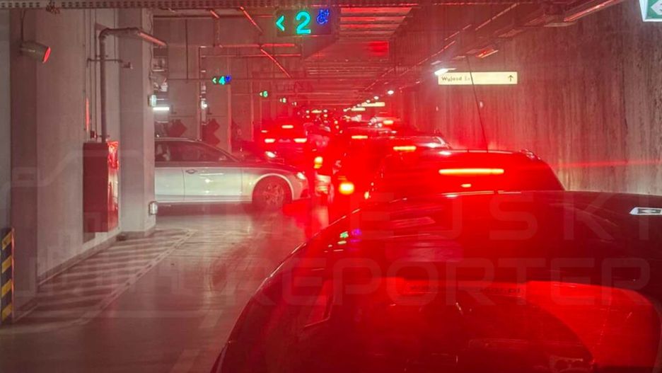 Kolejka samochodów oczekujących na wyjazd z podziemnego parkingu, oświetlona czerwonymi światłami.