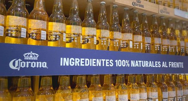 Butelki piwa Corona w kampanii ustawione odwrotnie na półkach sklepowych