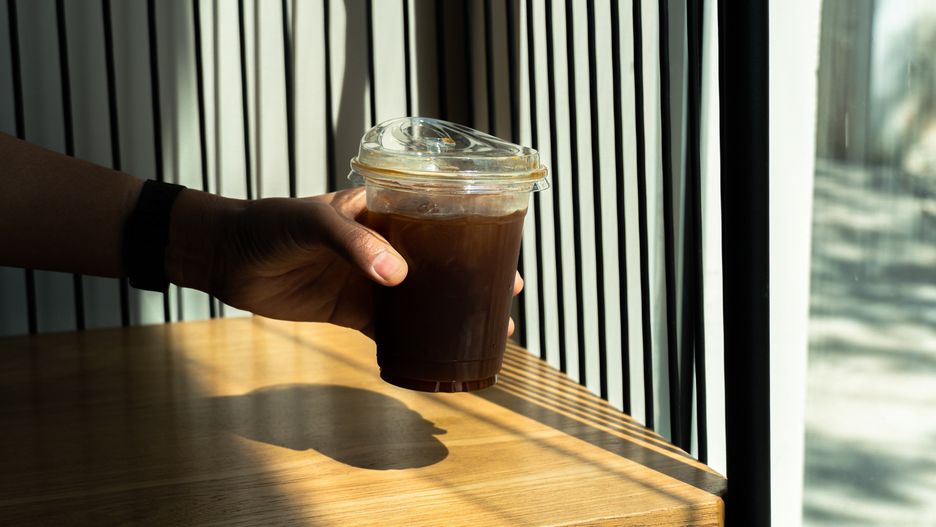 Hand holding black ice Coffee in drinking glass on wood table background with a sunbeam from the window. Summer refreshing drink. Black coffee in the morning with sunlight.
SandyHappy