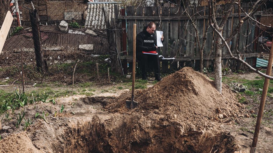 BUCHA, UKRAINE - APRIL 08: A policeman stands in front of an open grave in Bucha, Ukraine on April 08, 2022. (Photo by Diego Herrera Carcedo/Anadolu Agency via Getty Images)