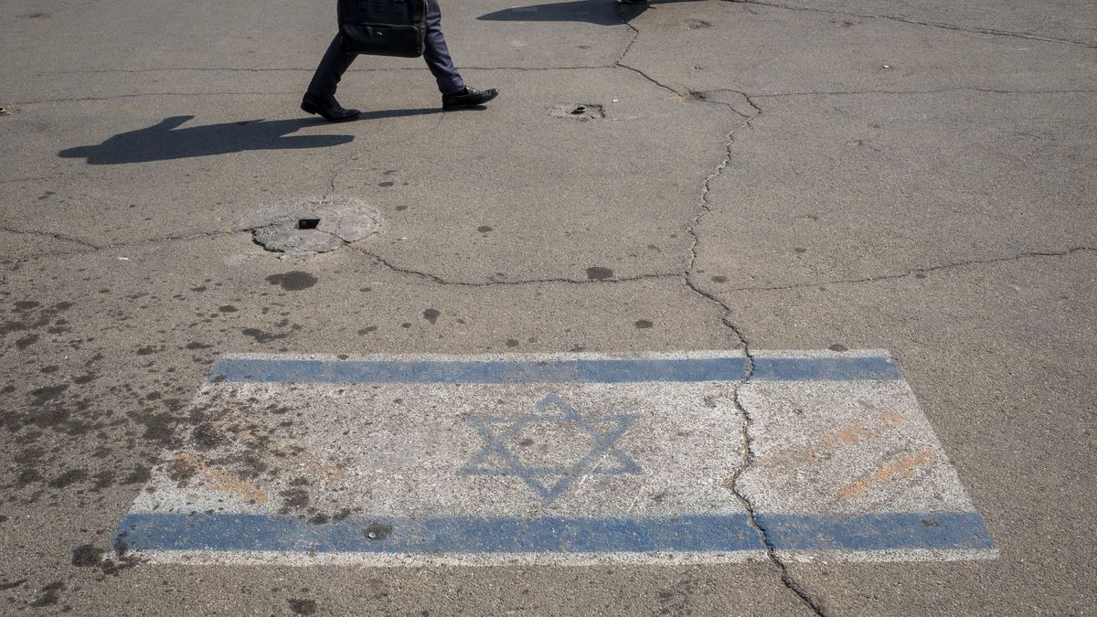 People are walking past an Israeli flag in downtown Tehran, Iran, on April 14, 2024. Iran is launching dozens of Unmanned Aerial Vehicles (UAVs) and missiles against Israel in response to the Israeli attack on its Consulate in Damascus. (Photo by Morteza Nikoubazl/NurPhoto via Getty Images)
