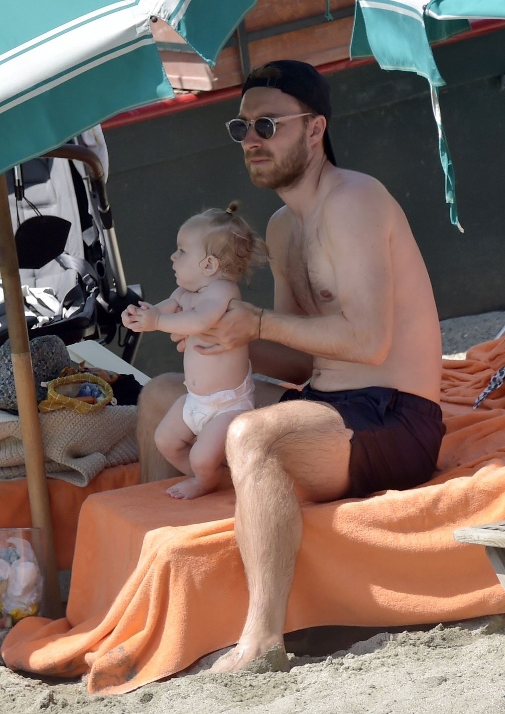 *EXCLUSIVE* Danish footballer Christian Eriksen with his wife Sabrina Kvist Jensen and their children on vacation in Portofino
portofino, ITALY  - *EXCLUSIVE*  - Danish footballer Christian Eriksen who suffered a cardiac arrest while playing for Denmark at Euro 2020 seems to have made a full recovery as he is seen with his wife Sabrina Kvist Jensen and their children enjoying a beach day in Portofino.

BACKGRID UK 15 AUGUST 2021,Image: 627240010, License: Rights-managed, Restrictions: RIGHTS: WORLDWIDE EXCEPT IN ITALY, Model Release: no, Credit line: Cobra Team / BACKGRID / Backgrid UK / Forum
Cobra Team / BACKGRID / Backgrid UK / Forum
Christian Eriksen, Black Cap, Nike, Brand, Facial Hair, Beard, Black Sunglasses, Shirtless, Bare Chest, Bare Chested, Black Shorts, Holding, Carrying, Baby, Cute, Barefoot, Football Player, Footballer, Holiday, Vacation, Enjoy, Enjoying