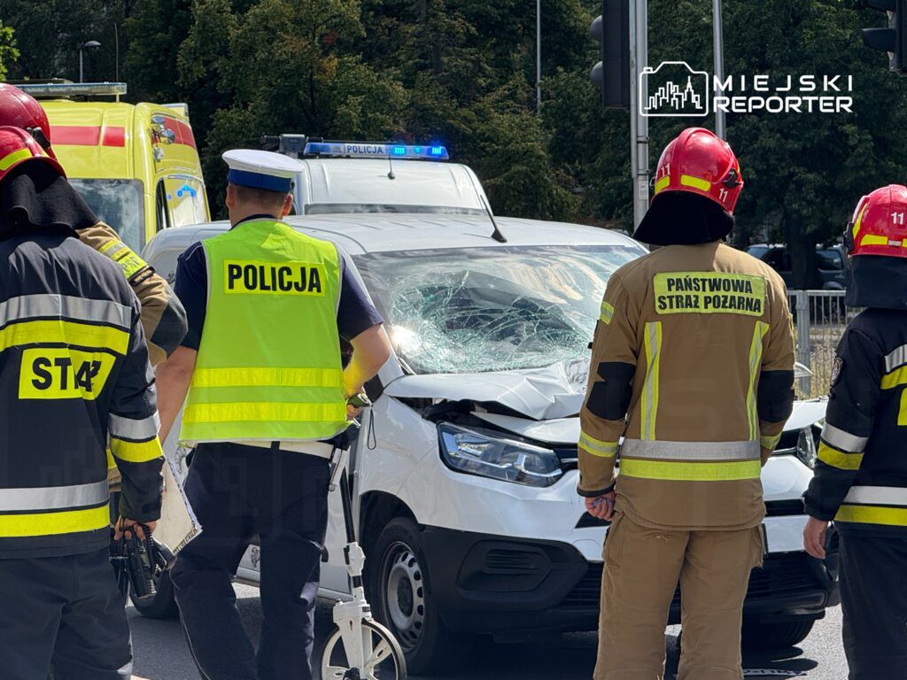 Grupa ratowników i policjantów ocenia uszkodzony samochód osobowy po wypadku drogowym.