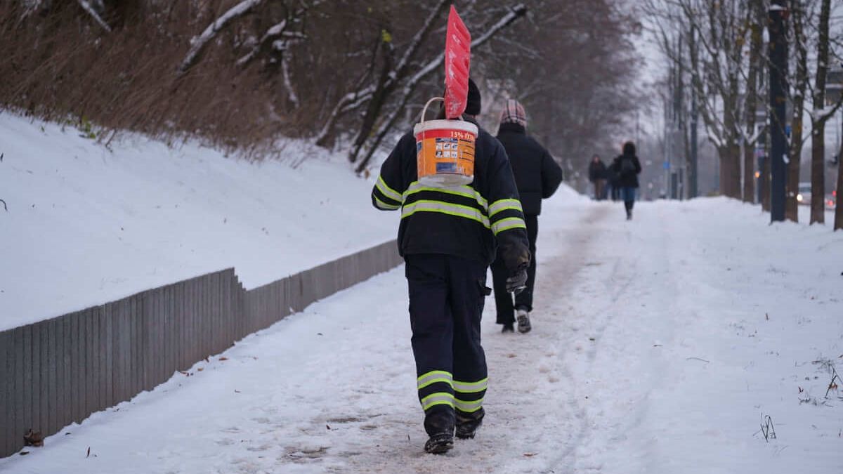 mężczyzna idący z łopatą do odśnieżania śnieg i wiaderkiem z piaskiem