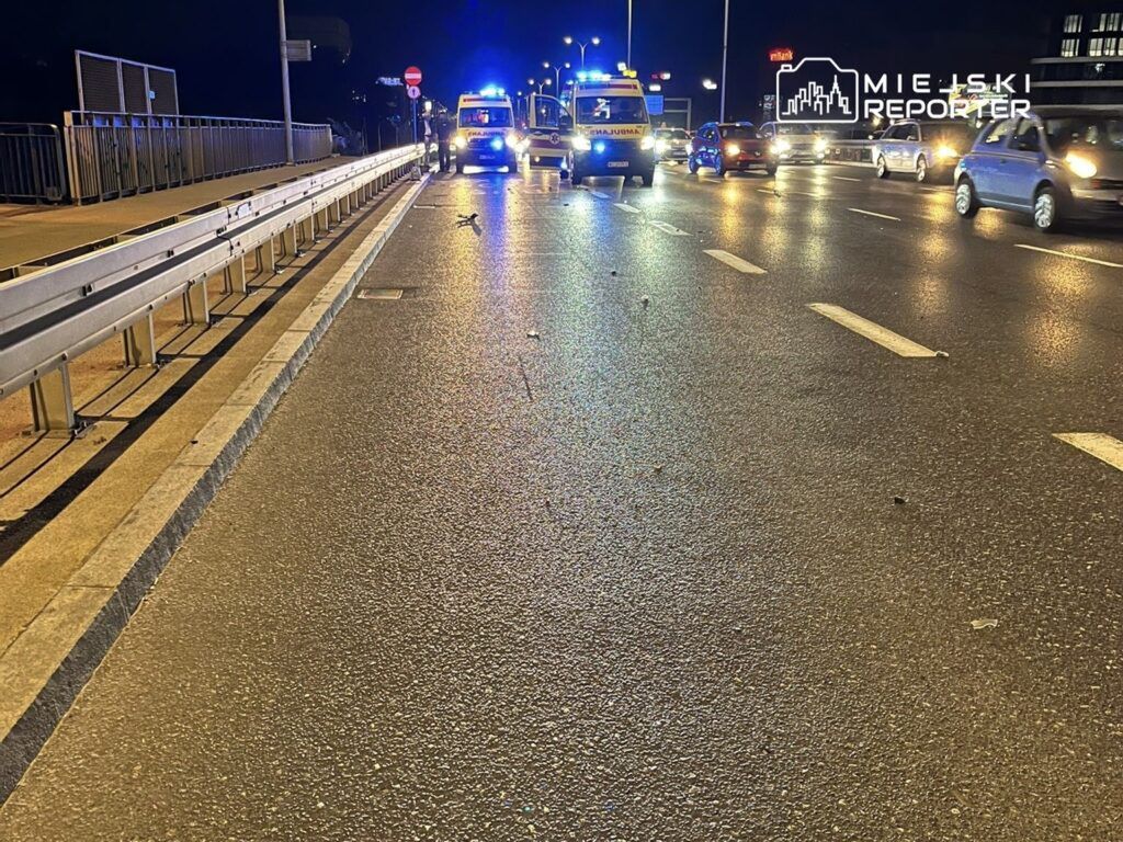 Na jezdni w nocy stoją karetki pogotowia, a w tle widać samochody poruszające się w obie strony.