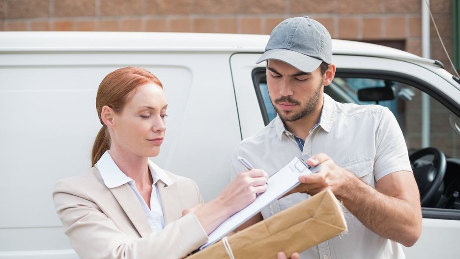Delivery driver handing parcel to customer outside van outside the warehouse