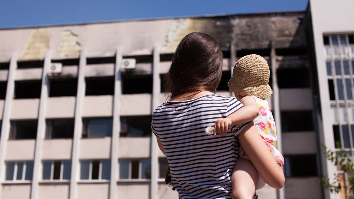 Matka z dzieckiem patrzy na spalony budynek ratusza w Mariupolu