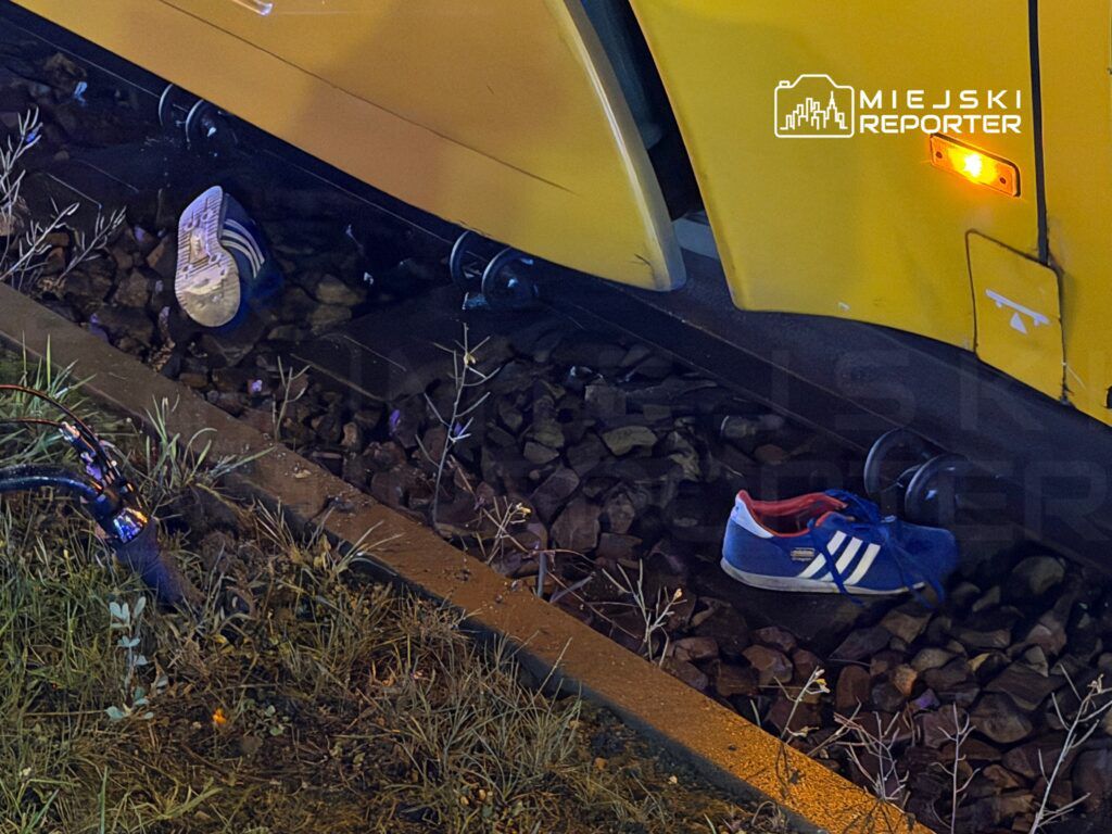 Na torach tramwajowych leżą dwa buty sportowe, jeden niebieski z białymi paskami, drugi czerwony z białymi detalami.