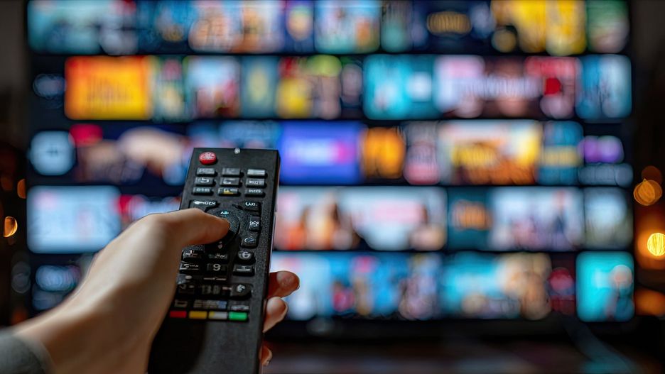 Hand holding remote control selecting media content on a large television screen