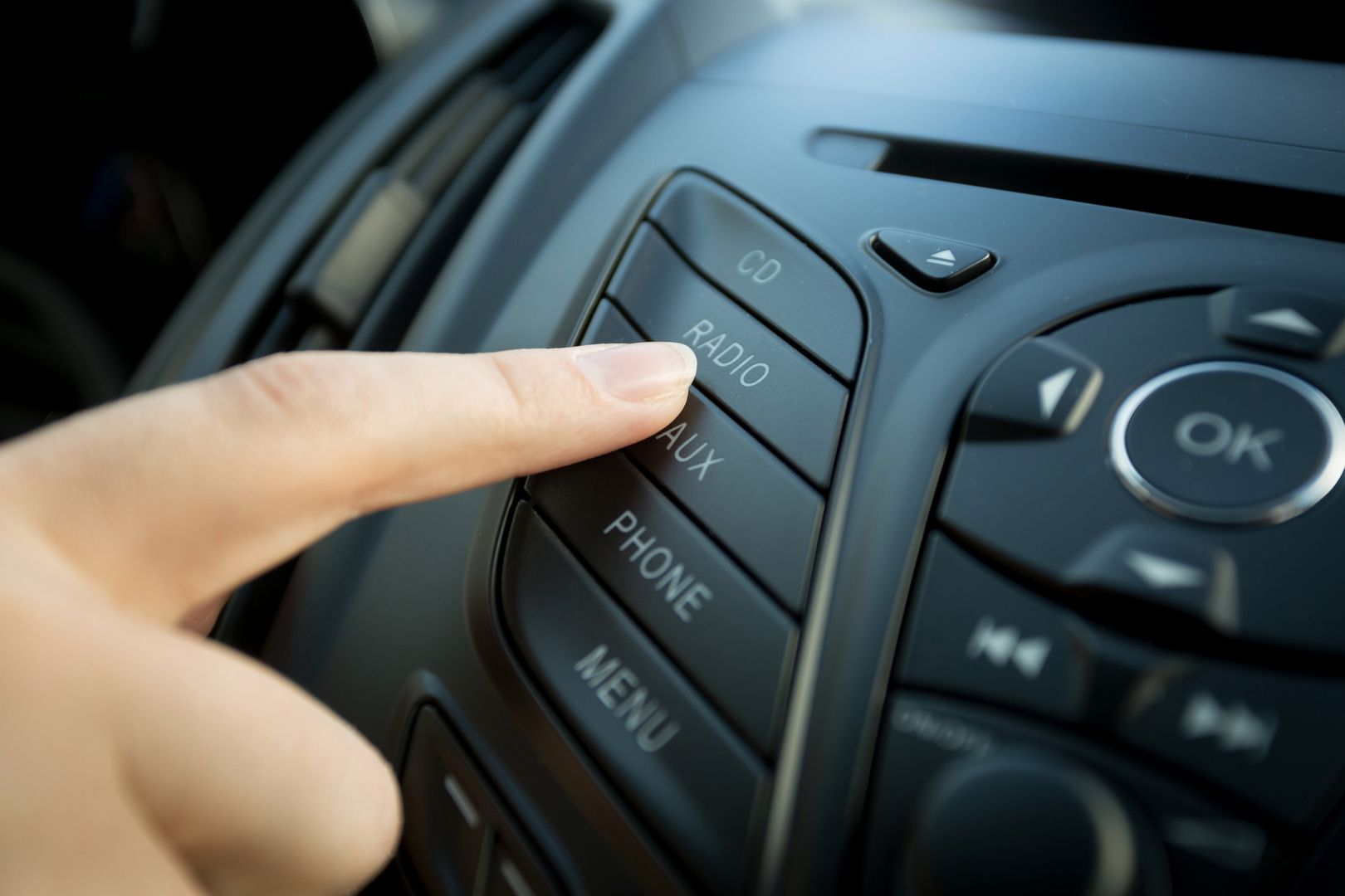 Closeup photo of female finger pressing radio button on car control panel