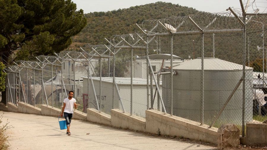 <<enter caption here>> at the Moria refugee camp on May 20, 2018 in Mytilene, Greece. Despite being built to hold only 2,500 people, the camp on the Greek island of Lesbos is home to over 6,000 asylum seekers who crossed the Aegean Sea from Turkey's nearby shore by boat, usually at night to avoid interception. Although the numbers of arrivals are lower than at the beginning of the crisis in 2015, when Syrians and Iraqis fled ISIS-controlled strongholds, boatloads of refugees from those countries and other troubled areas continue to land there, and critics say the local governments have yet to manage the situation, leading the squalid conditions at Moria to be seen as symbolic of poorly-managed policy. The camp, on the site of a former military base, is comprised of shipping containers, tents, and improvised shelters of wooden pallets and tarps, whose residents stranded there complain of poor food, power failures, disease, lack of medical care, and poisonous snakes as they wait to obtain transfer to the mainl
