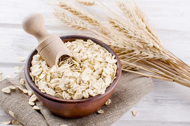 Oat flakes  in ceramic bowl and wooden spoon and spikelets on white vintage wooden background, selective focus copy space, top view