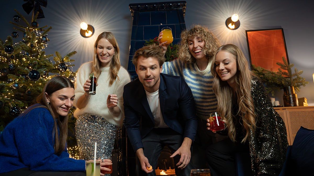  Grupa przyjaciół uśmiecha się i wspólnie bawi podczas świątecznego spotkania przy stole z napojami. - tytułowa