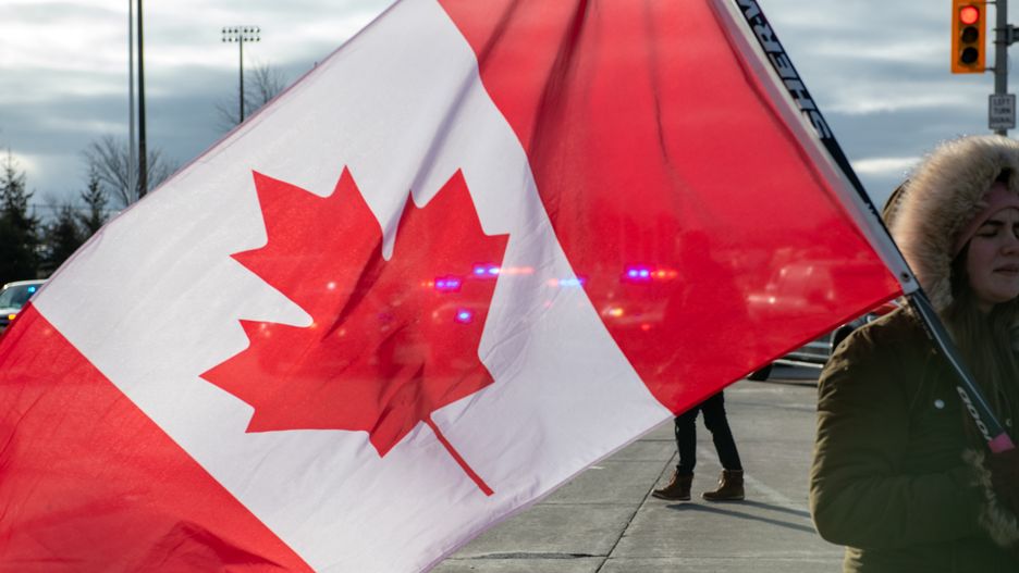 A protester blocking access to the Ambassador Bridge holds a Canadian flag after police moved in to clear the demonstration in Windsor, Ontario, Canada, on Saturday, Feb. 12, 2022. Police in Ontario have begun to clear out people who've been blocking the Ambassador Bridge that connects Canada with Detroit in a protest against Covid-19 restrictions. Photographer: Galit Rodan/Bloomberg via Getty Images
