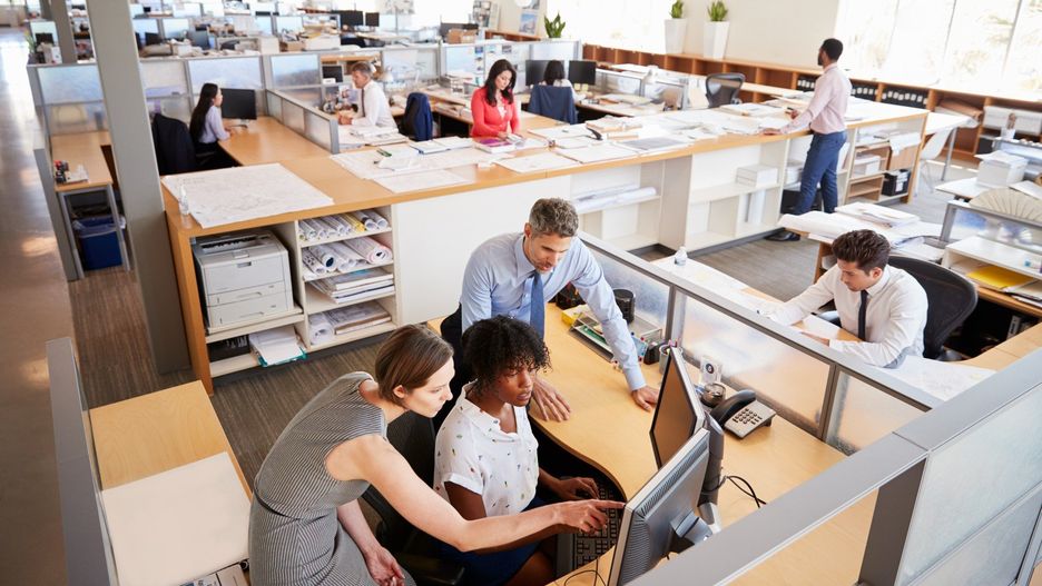Colleagues working at a womanâs workstation in a busy office