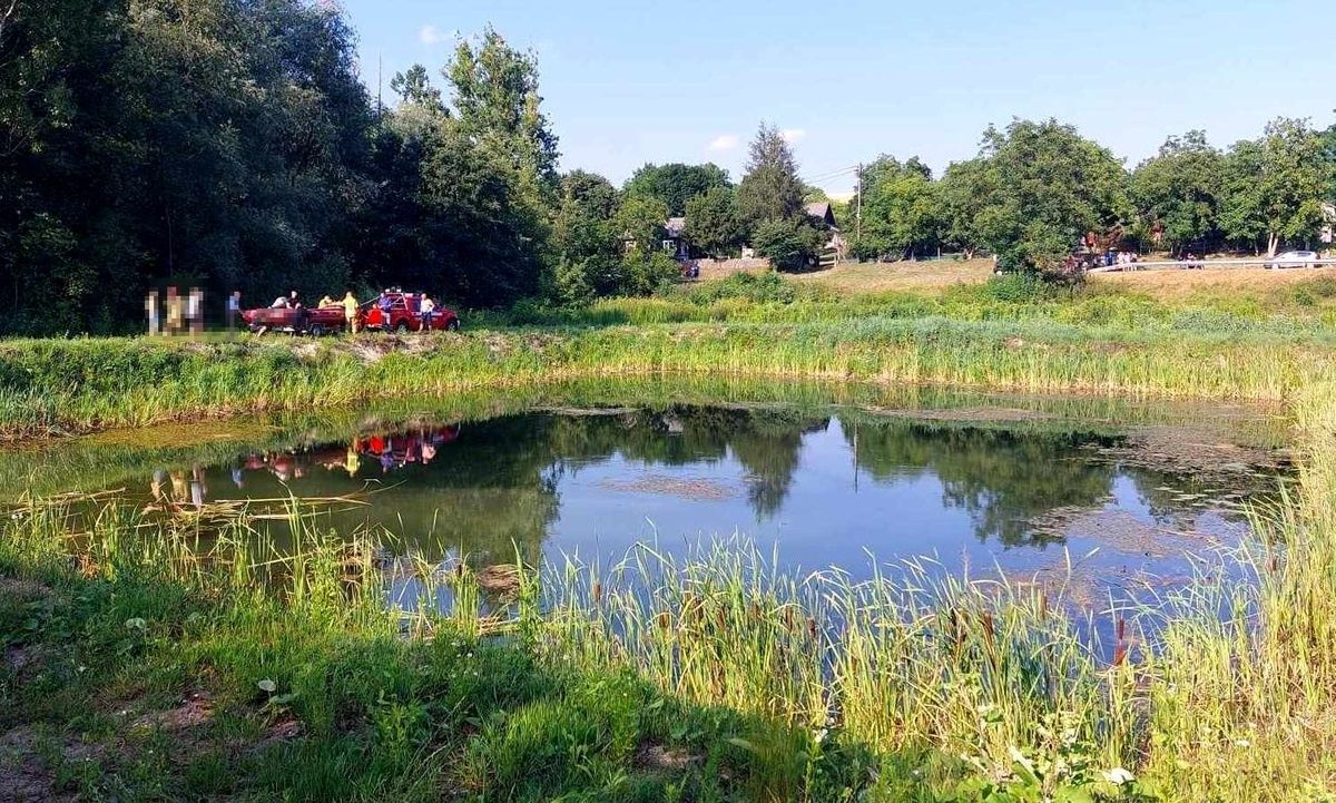 Staw, w tle stoją jednostki strazy pożarnej z łodzią