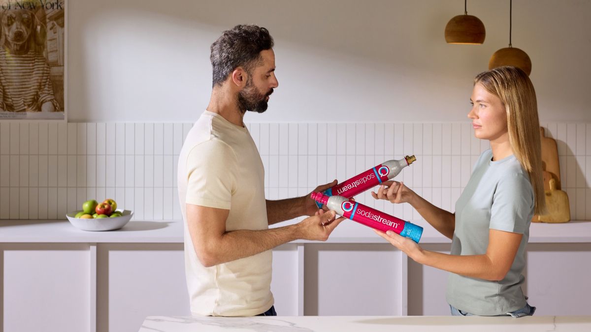  Mężczyzna i kobieta wymieniają między sobą różowe cylindry CO2 do saturatora SodaStream. 