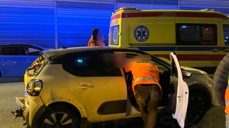 Osoby w pomarańczowych kamizelkach udzielają pomocy poszkodowanemu w wypadku drogowym przy uszkodzonym pojeździe.