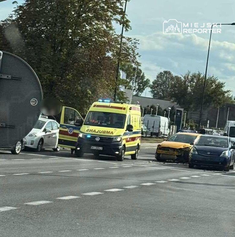 Karetka pogotowia z włączonymi sygnałami przy uszkodzonym samochodzie na ruchliwej drodze.