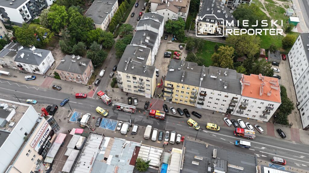Widok z lotu ptaka na ulicę z pojazdami ratunkowymi i strażackimi w akcji przed blokami mieszkalnymi.