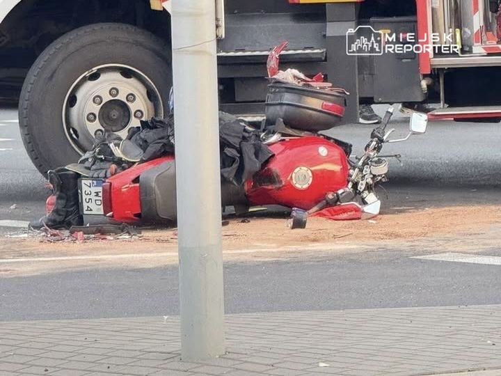Motocykl leżący na boku, obok dużego pojazdu ciężarowego, w miejskim otoczeniu.