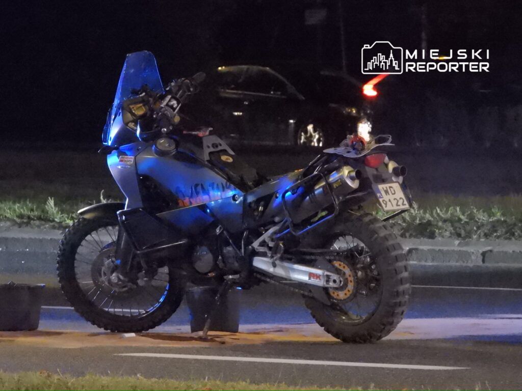 Motocykl terenowy zaparkowany na poboczu drogi, oświetlony niebieskimi światłami w nocy.