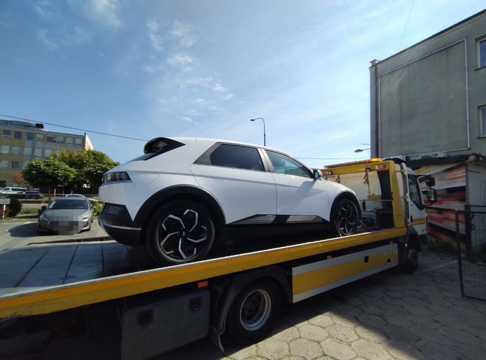 Nowoczesny samochód elektryczny załadowany na lawetę w miejskim otoczeniu.