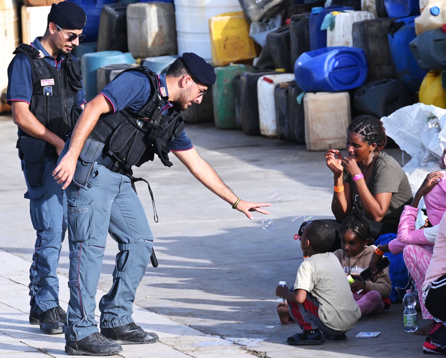 An Italian police officer interacts with a rescued migrant child blowing soap bubbles as a group waits for further registration procedures after arriving in the port of Lampedusa, 18 September 2023. More than 1,000 migrants remain in the hotspots of Lampedusa where they await transfer. Italian Deputy Premier and Foreign Minister Antonio Tajani on 15 September called for the intervention of the United Nations in response to the significant increase in the arrival of migrants and refugees by sea to Italy in recent days. EPA/CIRO FUSCO Dostawca: PAP/EPA.