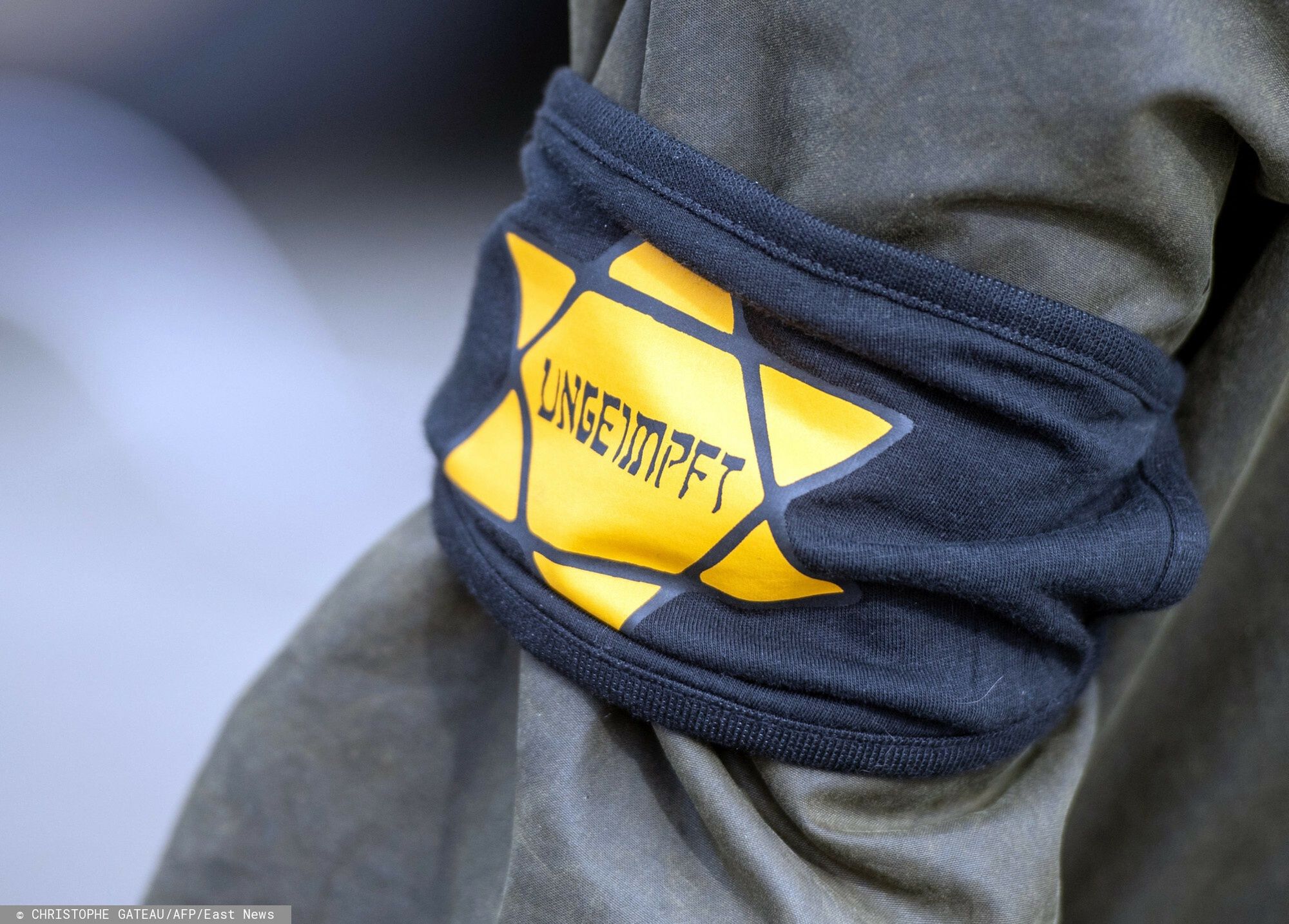 arch4805 April 2021, Berlin: At a demonstration against the restrictions imposed by the federal government's pandemic measures at the Brandenburg Gate, one participant wears an armband with a yellow star, reminiscent of a Jewish star, with the inscription "Unvaccinated". Photo: Christophe Gateau/dpa (Photo by Christophe Gateau / DPA / dpa Picture-Alliance via AFP)CHRISTOPHE GATEAU