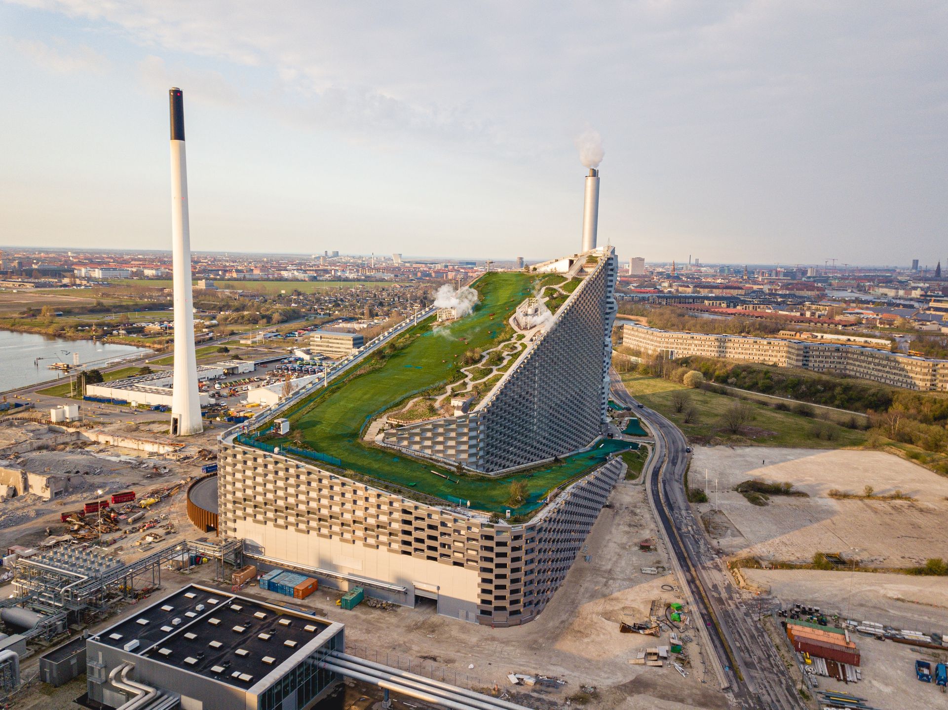 Amager Bakke in Copenhagen, DenmarkCopenhagen, Denmark - April 12, 2020: Aerial drone view of Amager Bakke, a waste to power plant with a ski slope on top.ski slope, amager bakke, Copenhagen, Denmark, skiing, power plant, copenhill, Bjarke Ingels, aerial, amager, amagerbakke, architecture, area, artificial, big, building, chimney, city, danish, drone, elevated, energy, environment, exterior, futuristic, green, group, high angle, incinerator, industrial, industry, landmark, management, metallic, modern, piste, rooftop, ski, sky, slope, smoke, sport, steam, surface, technology, urban, view, waste