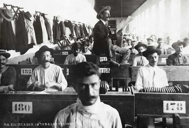 Lektor czytający niepiśmiennym pracownikom gazetę w fabryce kubańskich cygar (1900).