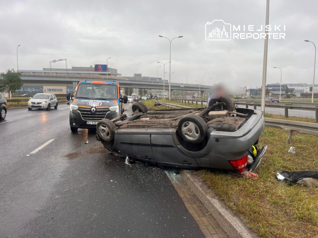 Z overturned vehicle on the roadside, emergency service vehicle parked nearby, traffic moving around the scene.
