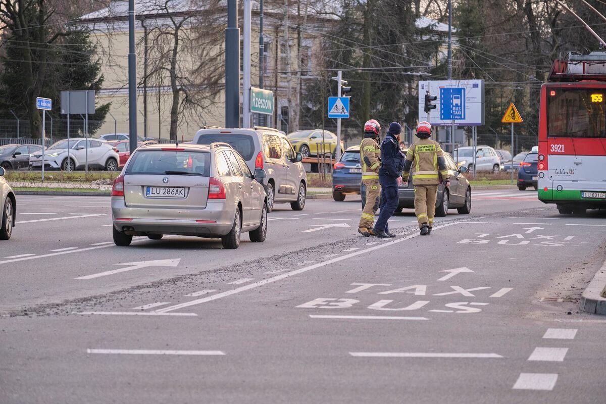 Dwóch strażaków i policjant idą wzdłuż ścieżki z betonu na jezdni