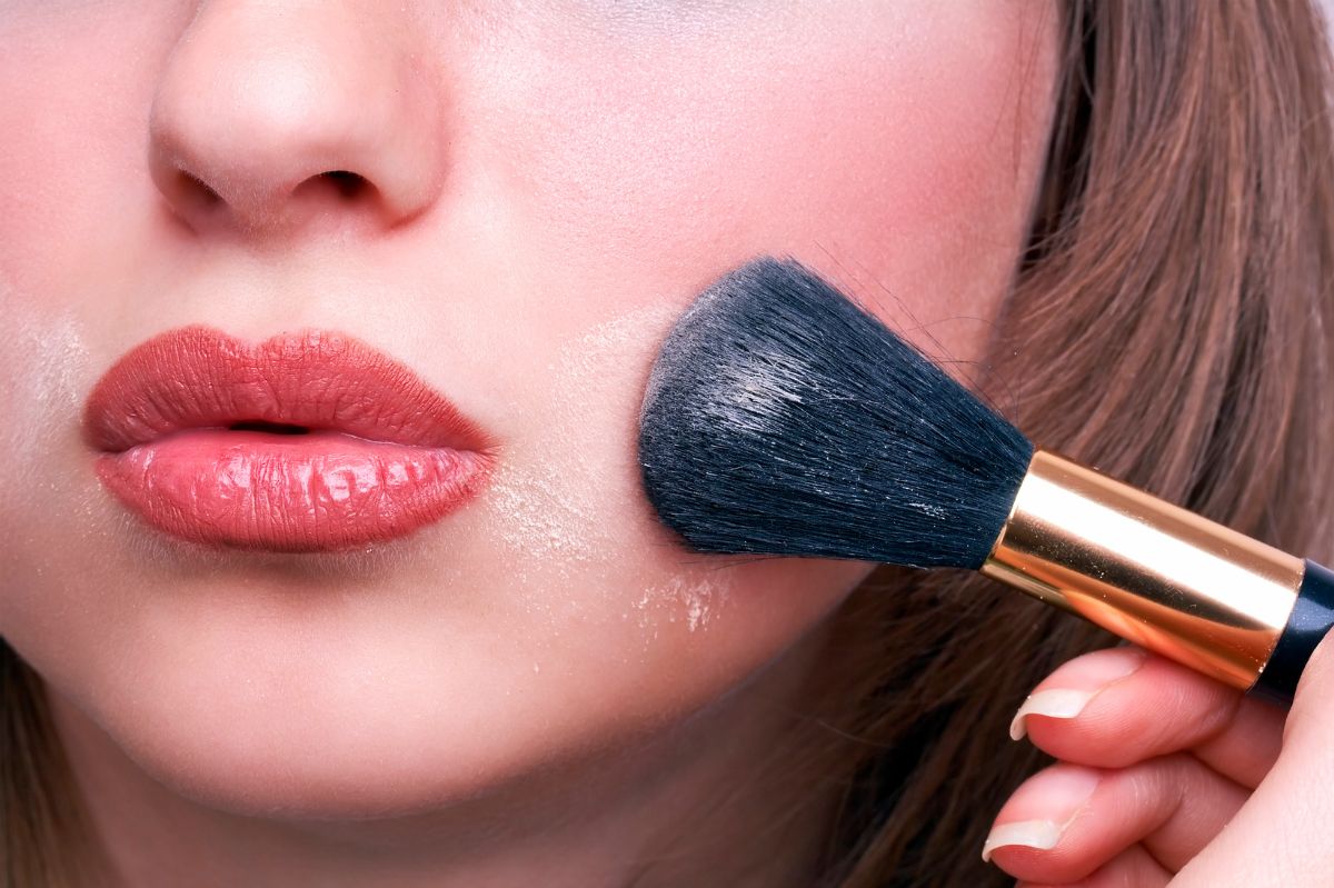 The woman applies cosmetics to her face with a brush.