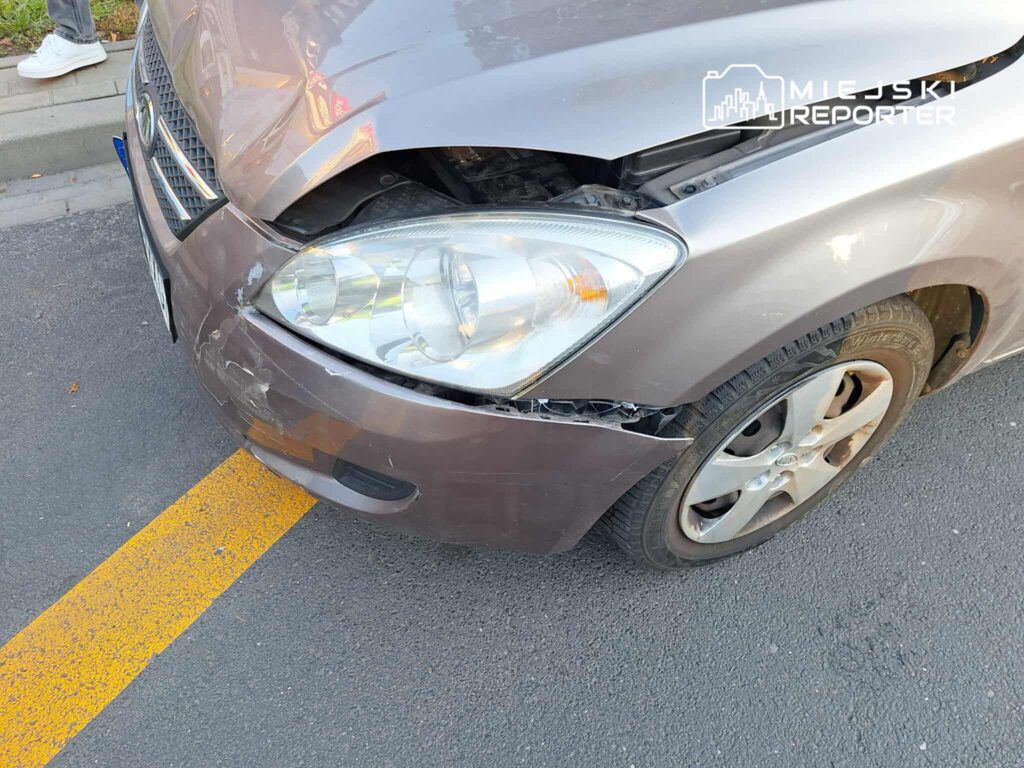 Uszkodzony samochód osobowy z wgniecioną maską i pękniętą karoserią stoi na ulicy obok krawężnika.