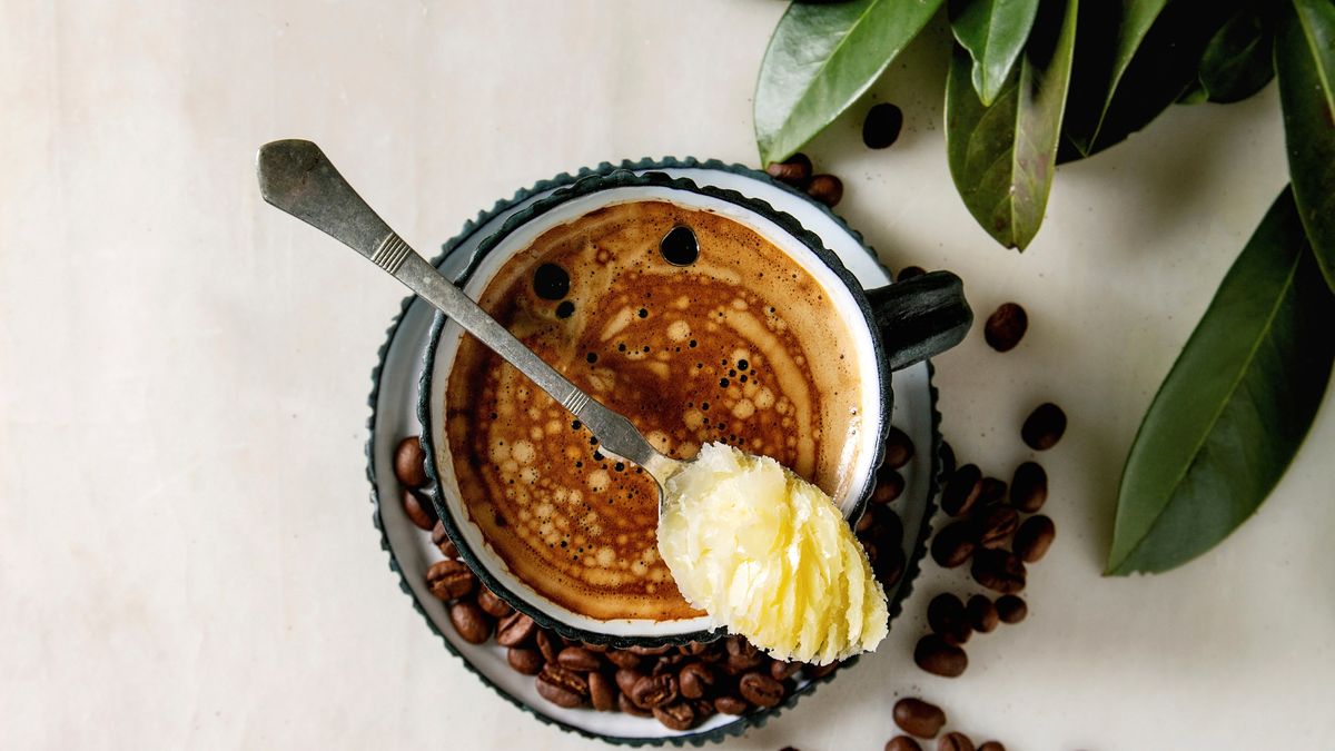 Bulletproof coffee. Keto diet coffee in blue ceramic cup with organic ghee butter in spoon with beans and green branch over white marble background. Flat lay. spaceBulletproof coffee. Keto diet coffee in blue ceramic cup with organic ghee butter in spoon with beans and green branch over white marble background. Flat lay. space. (Photo by: Natasha Breen/REDA&CO/Universal Images Group via Getty Images)REDA&CObackground, black, blended, branch, ceramic, coffee, diet, energy, fat, green, health, healthy, keto, ketogenic, lay, leaves, marble, melted, oil, overhead, paleo, proof, space, top, view, white