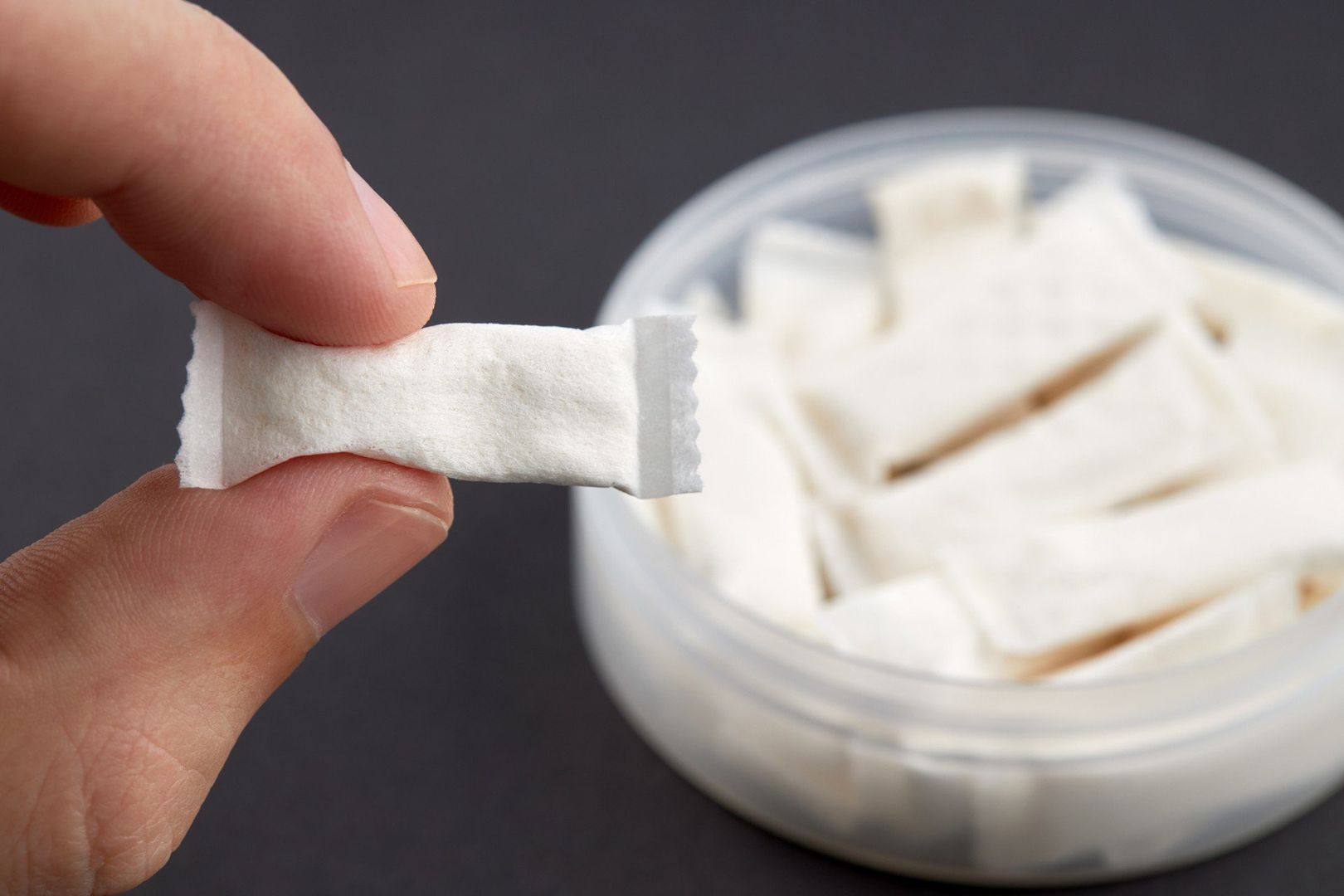 caucasian person holds snus tobacco pouch over black background. copy space. alternative chewing nicotine smoking.