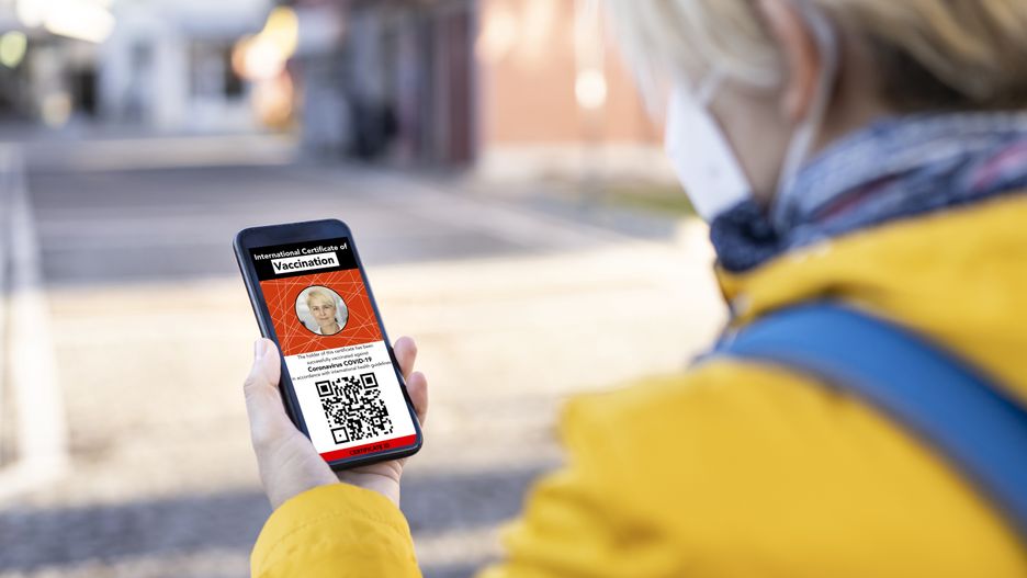 A young woman checking her digital international certificate of COVID-19 Vaccination, standing on the street, wearing a FFP2 Mask