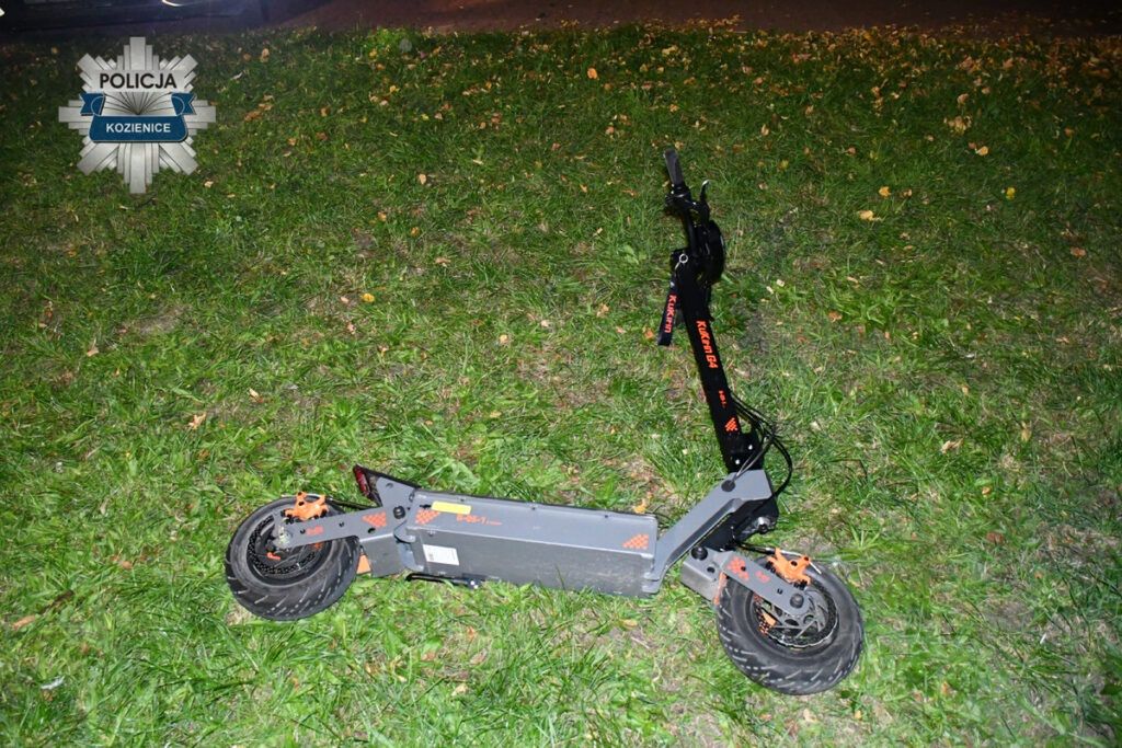 Złoty skuter elektryczny leży na trawie w nocy, obok widocznego fragmentu drogi.