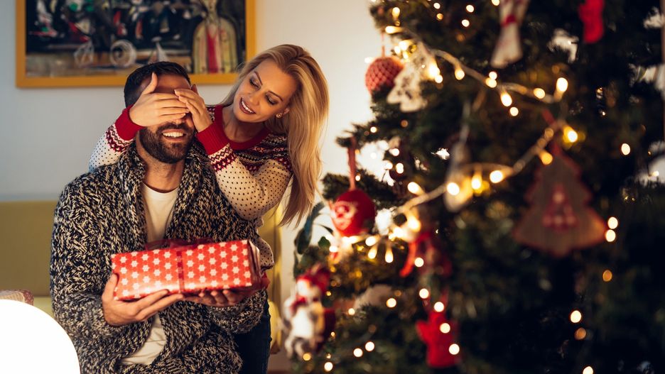 Beautiful girl surprising her boyfriend with a present.Bernard Bodochristmas, couple, gift, present, happy, people, man, surprise, presents, woman, new, tree, year, gifts, young, love, person, together, home, xmas, smile, girlfriend, happiness, two, celebration, girl, family, beautiful, holiday, female, fun, portrait, lifestyle, holding, open, romantic, exchanging, giving, celebrating, winter, christmas tree, new year, decoration, joy