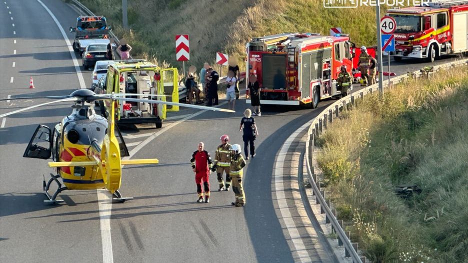 Na autostradzie lądował śmigłowiec ratunkowy, obok stoją strażacy i ratownicy medyczni, a w tle widać pojazdy służb.