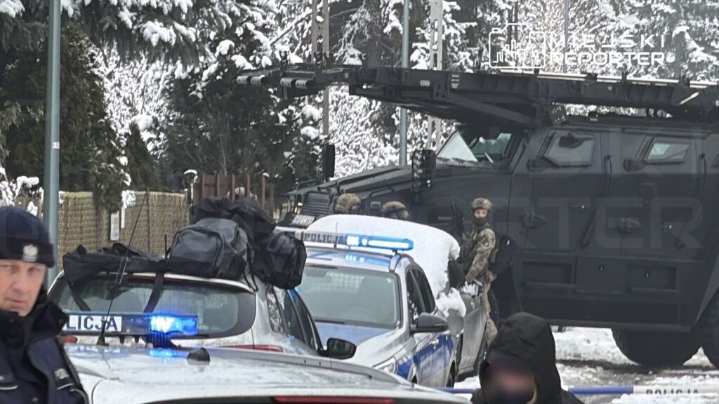 Grupa uzbrojonych policjantów w mundurach stoi obok opancerzonego pojazdu w zaśnieżonym otoczeniu.