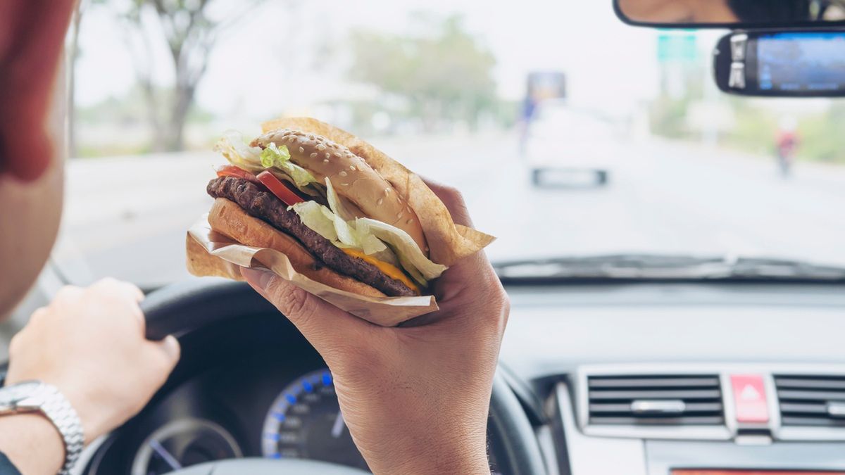 Mężczyzna je burgera podczas prowadzenia samochodu.