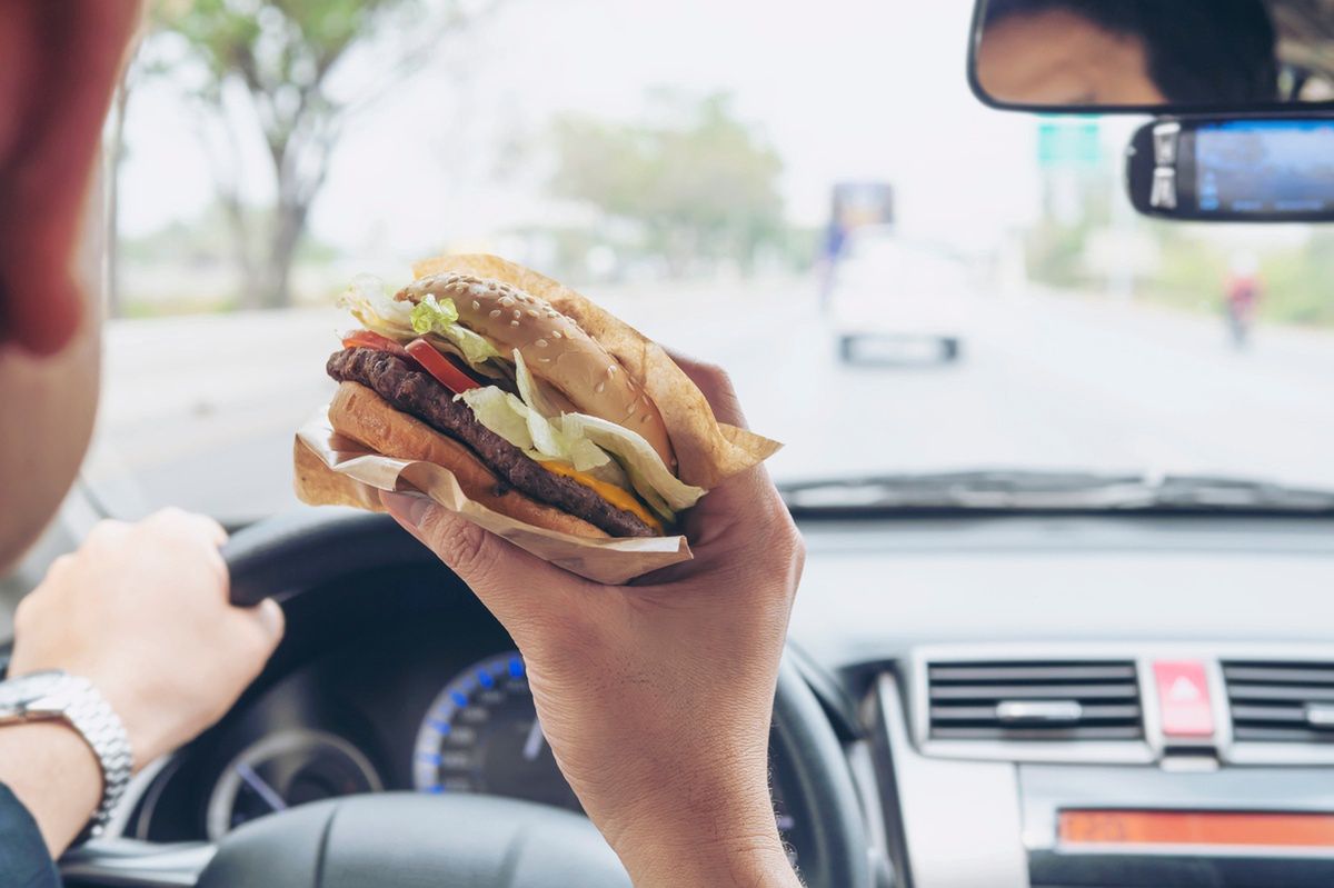 Mężczyzna je burgera podczas prowadzenia samochodu