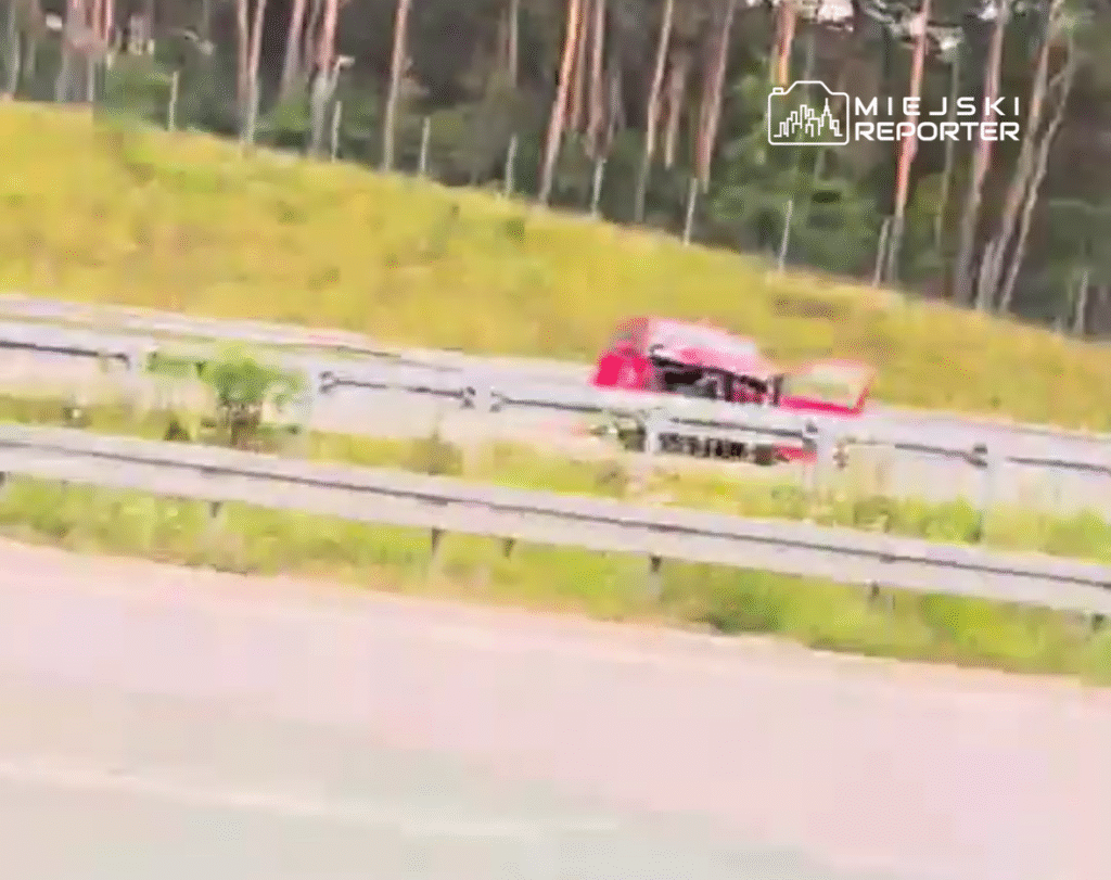 Czerwony samochód osobowy z otwartą maską stoi na poboczu drogi w otoczeniu lasu.