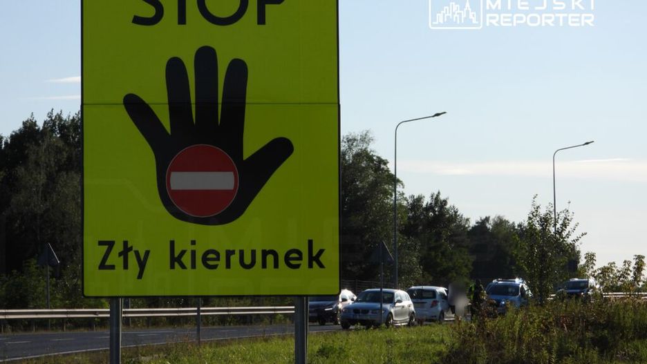 Żółty znak drogowy z napisem "STOP" i symbolem zakazu wjazdu informuje o złym kierunku na drodze.