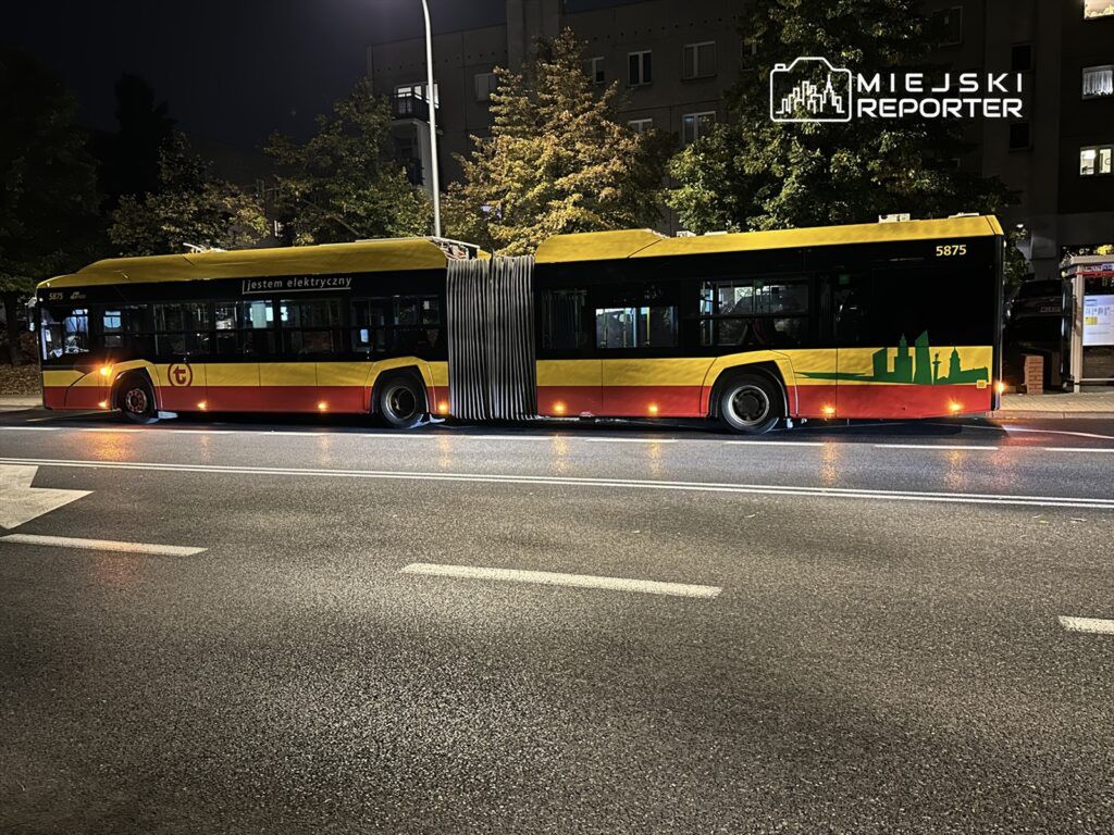 Elektryczny autobus z przeszkloną karoserią i żółto-czerwonym malowaniem stoi na ulicy w nocy.