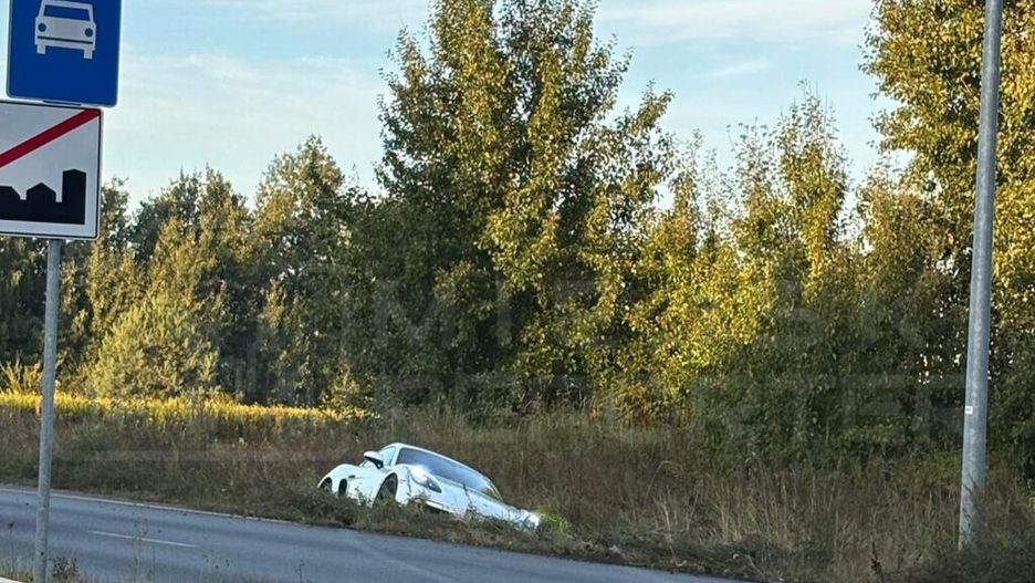 Biały samochód osobowy utknął w zaroślach przy drodze, obok znaków drogowych z ograniczeniem prędkości.
