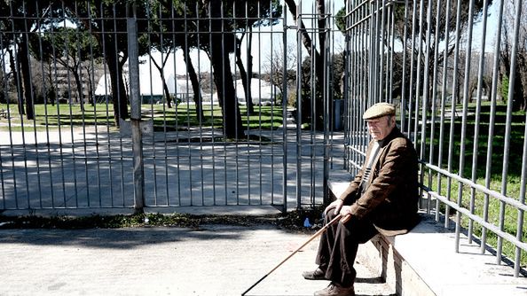 Zdjęcie poglądowe. Starszy mężczyzna siedzi przed jednym z parków w Rzymie. 