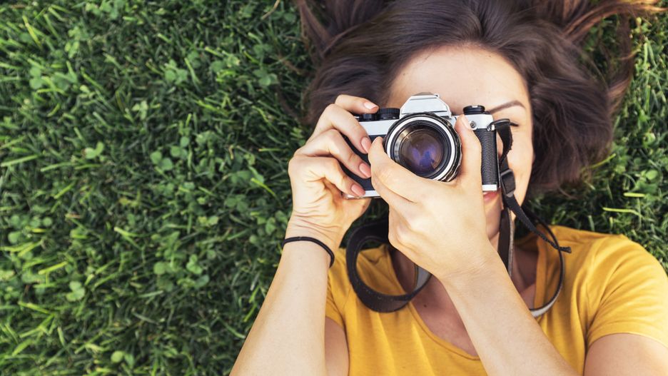 Smiling young woman using a camera to take photo at the park.
